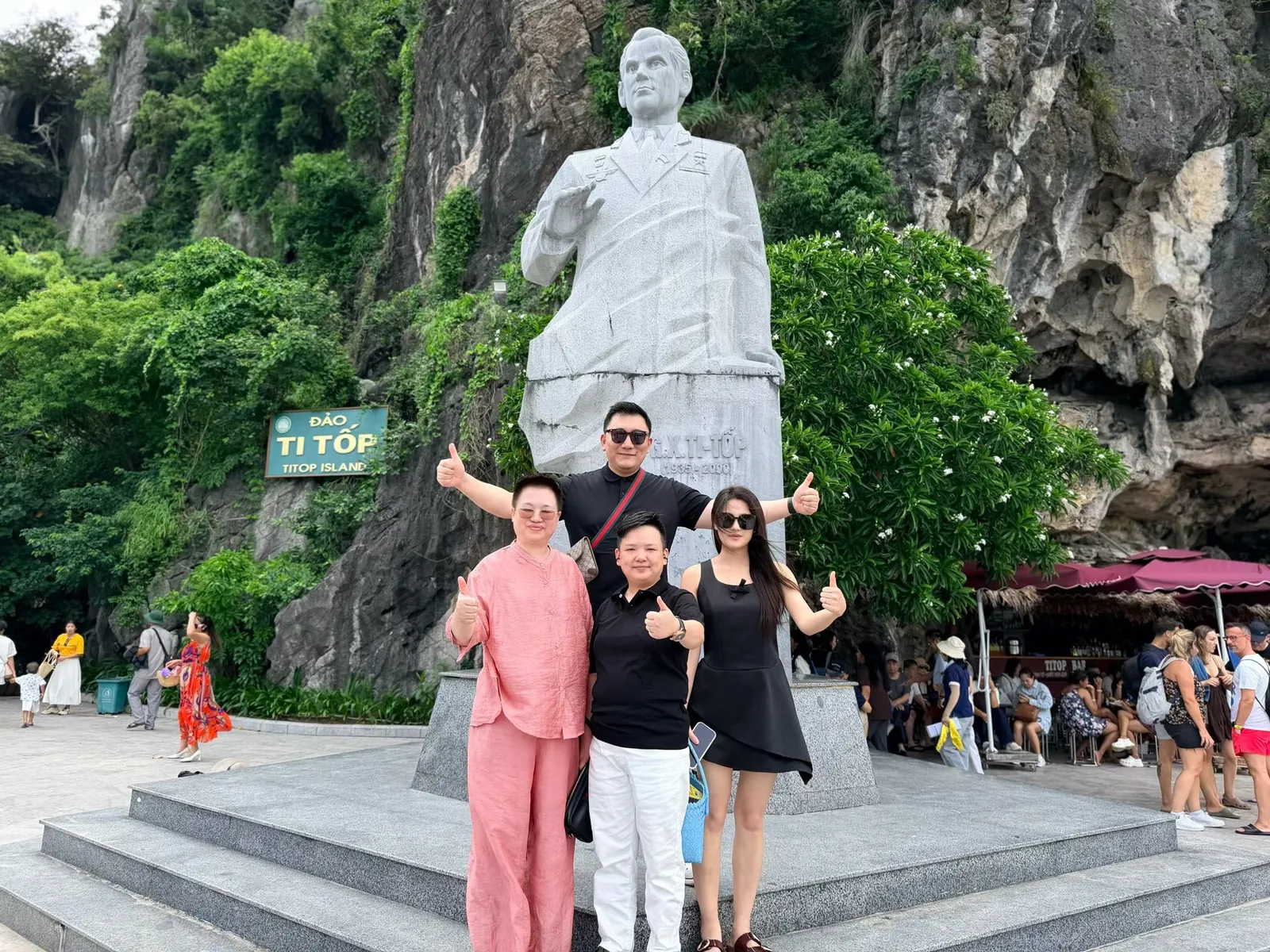 四人在 TITOP 岛季托夫雕像前竖起大拇指合影,背后是长满绿树的石灰岩山壁